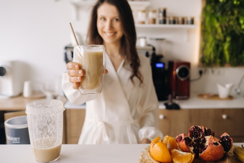 happy smiling healthy woman has prepared fruit cocktail gives it you while standing home kitchenhealthy eating